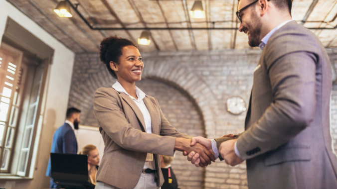 Woman and man shaking hands in a brick-lined room with a window.