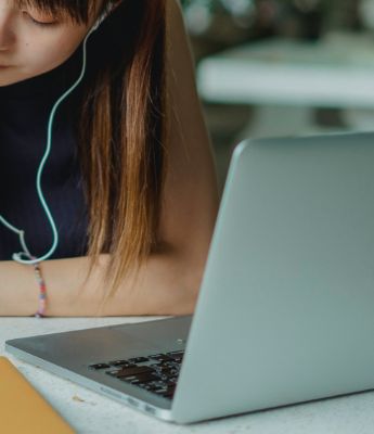 Student with headphones working at a desk with laptop computer.