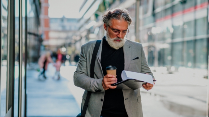 Man standing on a city street reading holding a beverage.